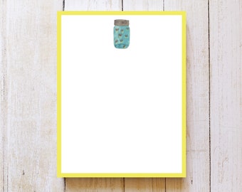 May include: A yellow notepad with a light blue mason jar with a brown lid and a white background. The mason jar has a pattern of small black dots.