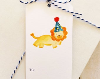 May include: A white gift tag with a lion wearing a blue and yellow party hat with a red pom-pom. The tag has the words "TO:" and "FROM:" printed on it.