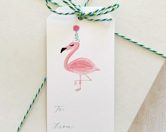 May include: Pink flamingo gift tag with a party hat and flowers on top. The tag has the words "To:" and "From:" written on it.