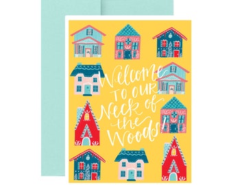 May include: A yellow card with a welcome message that says "Welcome to our Neck of the Woods". The card is decorated with colorful illustrations of houses.