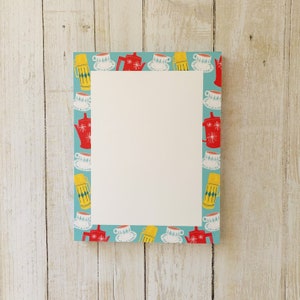 May include: A blue and white notepad with a border of red teapots, yellow thermoses, and white teacups. The border is on a light blue background.