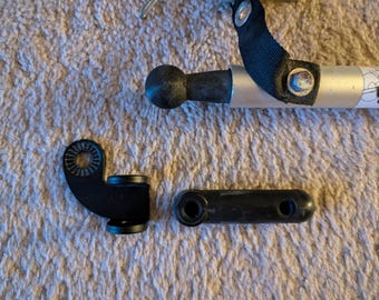 Può includere: Una collezione di parti nere per rimorchio per biciclette, tra cui un gancio di traino, una biella e uno snodo sferico. Le parti sono realizzate in metallo e plastica e sono progettate per collegare un rimorchio a una bicicletta.