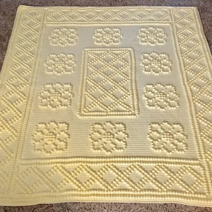 May include: A yellow crocheted blanket with a textured pattern of flowers and diamonds. The blanket is made with a soft, fluffy yarn.