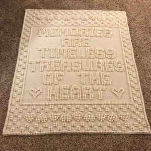 Peut inclure: Une couverture en crochet blanche avec le texte "Memories are the Timeless Treasures of the Heart" en lettres en relief.