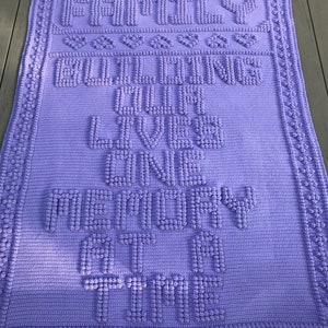May include: Purple crochet blanket with the text "Family Building Lives One Memory At A Time" in raised letters.