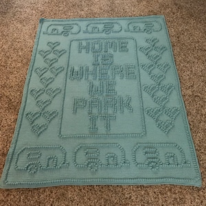 May include: A light blue crocheted blanket with the text "Home is where the park is" and "Go Green" in raised lettering.