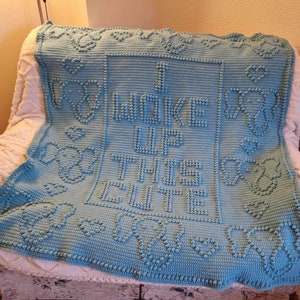 以下が含まれることがあります： 正方形の枠の中に「I woke up and this is cute」という文字が書かれた、薄い青色の編み物の毛布です。