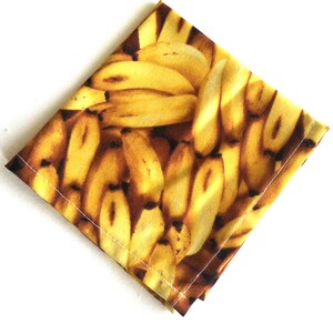 May include: A yellow fabric napkin with a print of a bunch of bananas.