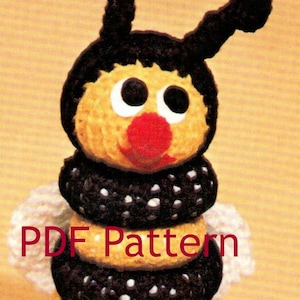 May include: A crocheted bee toy with black and yellow stripes, white polka dots, and a red nose. The bee is sitting on a red and green flower.