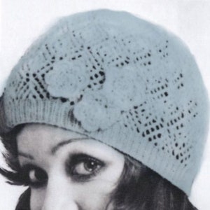 May include: A light blue knitted hat with a lacy design and floral embellishments.