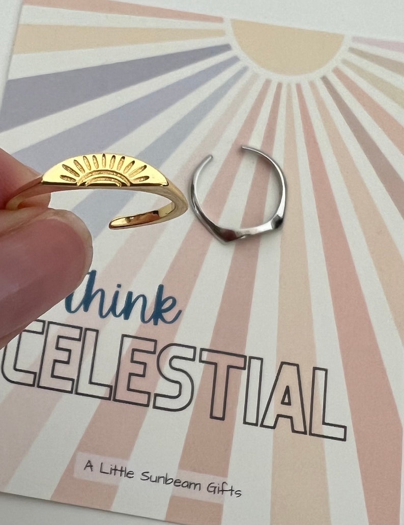 May include: Two gold toe rings, one with a sun design and the other a simple band. The rings are on a card with the text "Think Celestial" and "A Little Sunbeam Gifts".
