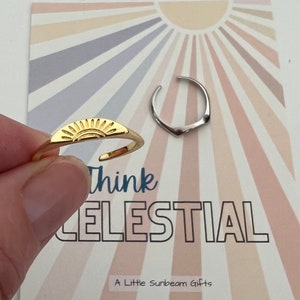 May include: Two gold rings with a sun and a crescent moon design. The rings are on a card with a sunburst background and the text "Think Celestial" and "A Little Sunbeam Gifts".