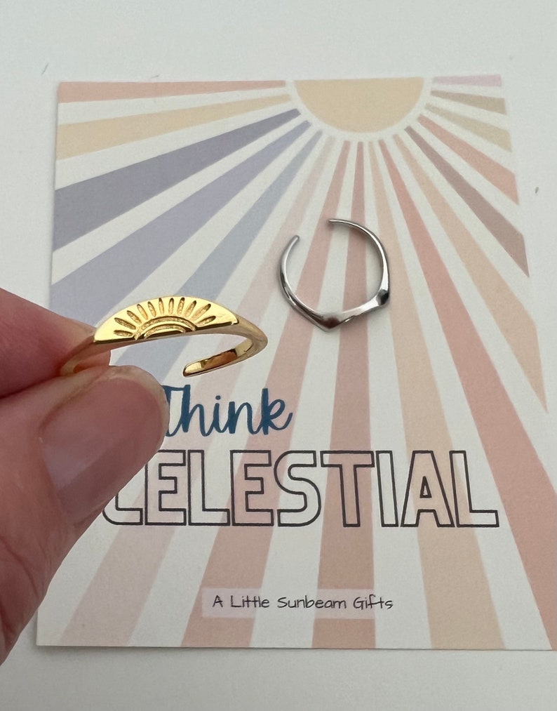 May include: Two gold rings with a sun and a crescent moon design. The rings are on a card with a sunburst background and the text "Think Celestial" and "A Little Sunbeam Gifts".