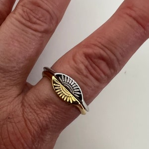 May include: A gold and silver ring with a sun design. The ring is worn on a finger.