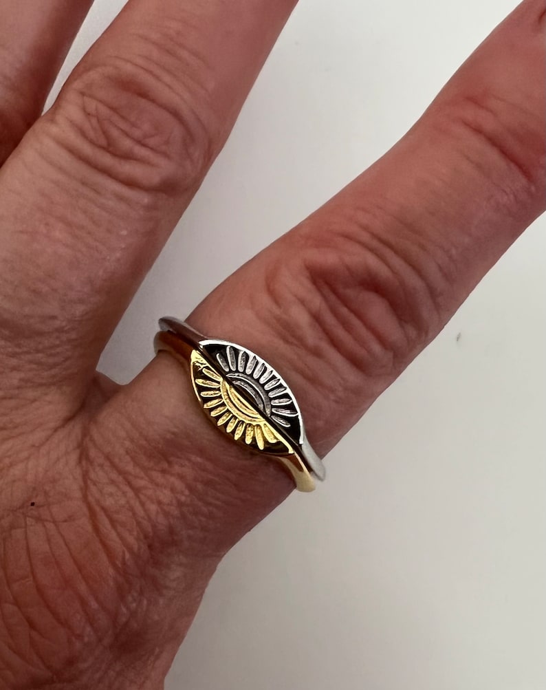 May include: A gold and silver ring with a sun design. The ring is worn on a finger.