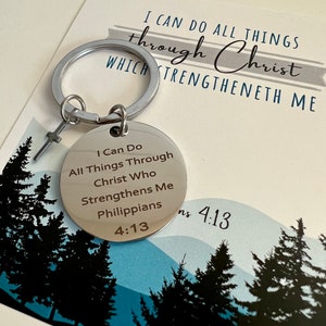 May include: A silver keychain with a round charm that says "I Can Do All Things Through Christ Who Strengthens Me Philippians 4:13". The keychain is on a white background with a blue and green image of trees.