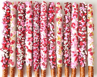 May include: A dozen chocolate-covered pretzels dipped in white and milk chocolate and decorated with pink and red sprinkles and heart-shaped sprinkles.
