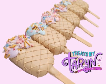 May include: A row of ice cream-shaped treats on wooden sticks. The treats are light brown with a waffle pattern and topped with pastel-colored frosting and sprinkles. The treats are arranged diagonally against a light pink background. The logo "Treats by Taryn" is in the bottom right corner.