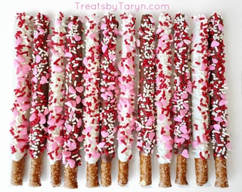 May include: A dozen chocolate-covered pretzel sticks dipped in white and dark chocolate and decorated with red and pink sprinkles and heart-shaped sprinkles. TreatsbyTaryn.com