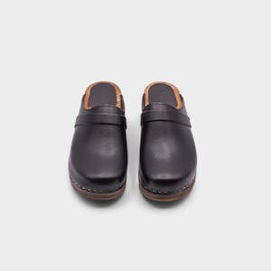 Malmö-style clogs designed by Sandgrens in classic black leather. Featuring a smooth, slip-on design with a supportive strap for stability. The sturdy wooden sole and hand-stapled construction ensure durability and all-day comfort, making them a stylish and functional footwear choice.