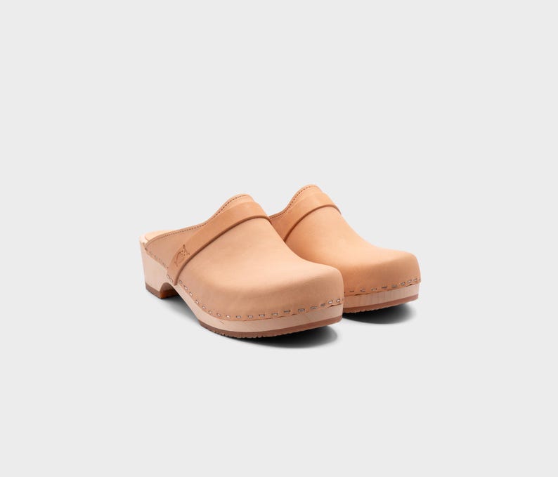 Malmö-style clogs designed by Sandgrens in classic Ecru Beige  leather. Featuring a smooth, slip-on design with a supportive strap for stability. The sturdy wooden sole and hand-stapled construction ensure durability and all-day comfort, making them a stylish and functional footwear choice.