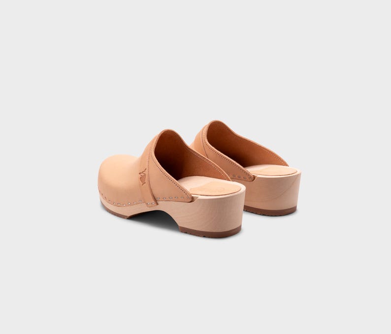 Malmö-style clogs designed by Sandgrens in classic Ecru Beige  leather. Featuring a smooth, slip-on design with a supportive strap for stability. The sturdy wooden sole and hand-stapled construction ensure durability and all-day comfort, making them a stylish and functional footwear choice.