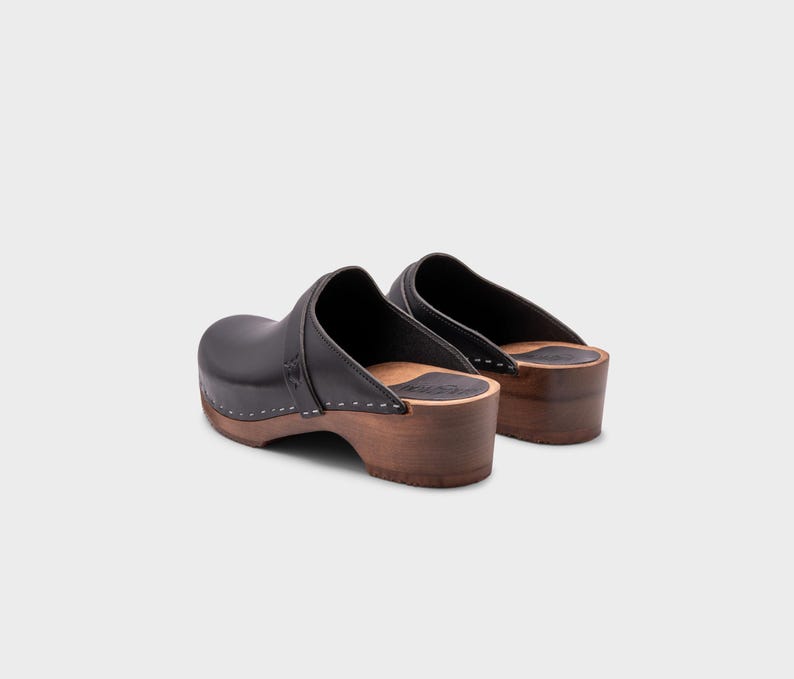 Malmö-style clogs designed by Sandgrens in classic black leather. Featuring a smooth, slip-on design with a supportive strap for stability. The sturdy wooden sole and hand-stapled construction ensure durability and all-day comfort, making them a stylish and functional footwear choice.