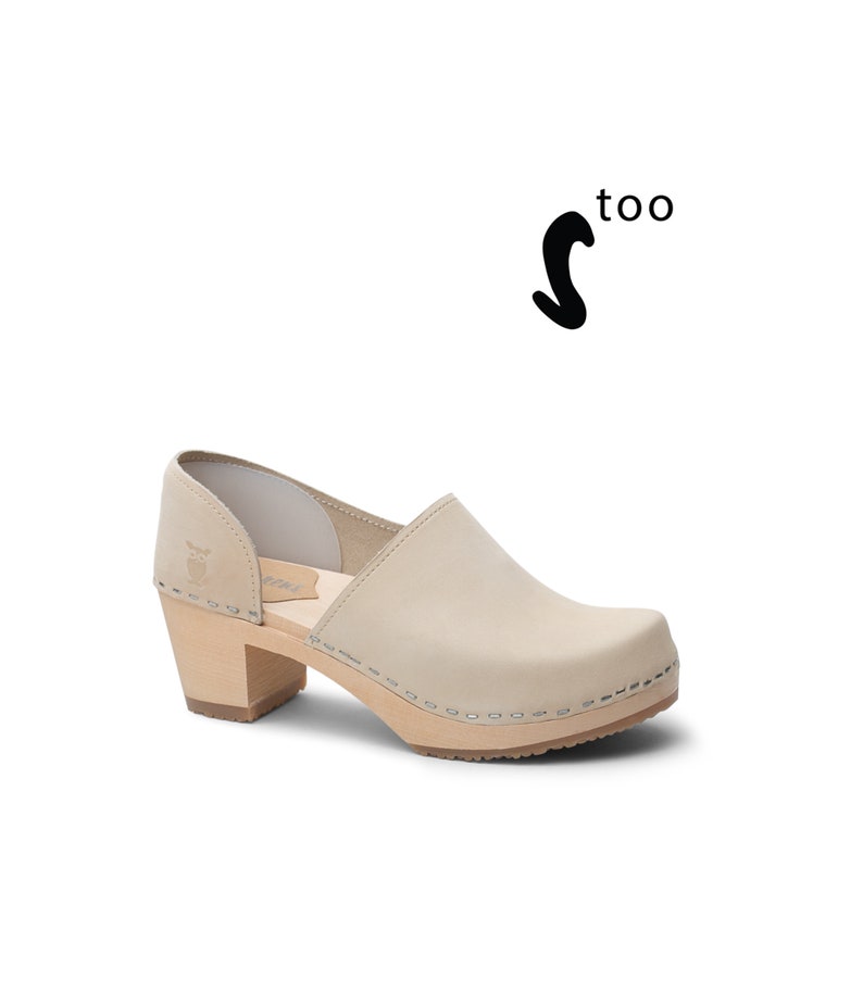 Puede incluir: Un par de zuecos de tac&oacute;n de cuero beige con un detalle de corte en el lateral. Los zuecos tienen un tac&oacute;n y una suela de madera.