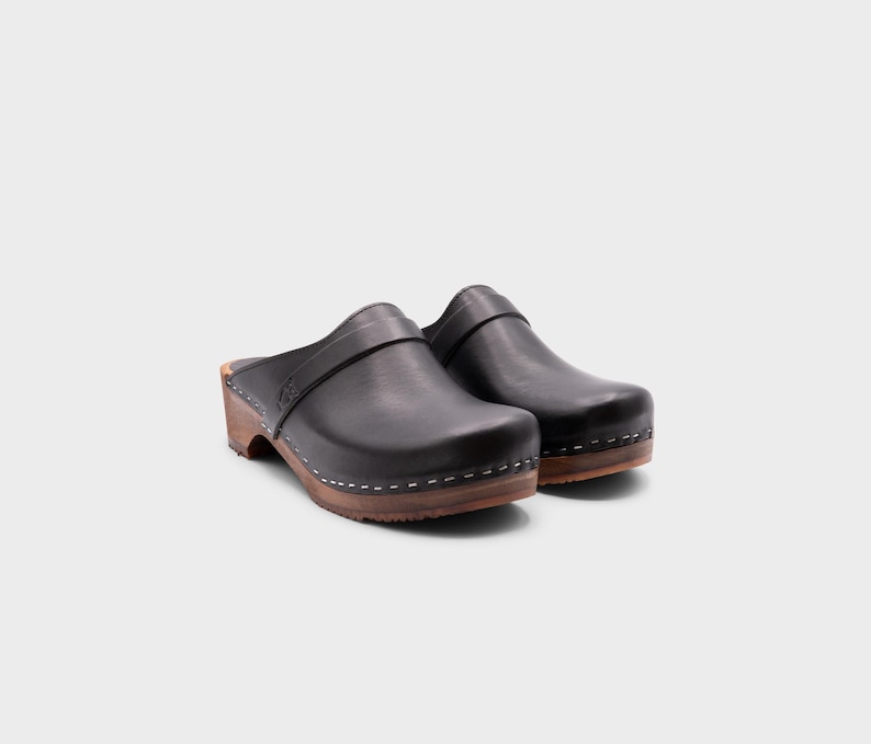 Malmö-style clogs designed by Sandgrens in classic black leather. Featuring a smooth, slip-on design with a supportive strap for stability. The sturdy wooden sole and hand-stapled construction ensure durability and all-day comfort, making them a stylish and functional footwear choice.