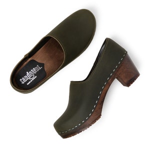 high heeled closed-back clogs in dark green leather on a dark wooden base