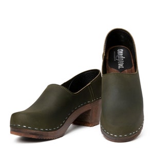 high heeled closed-back clogs in dark green leather on a dark wooden base