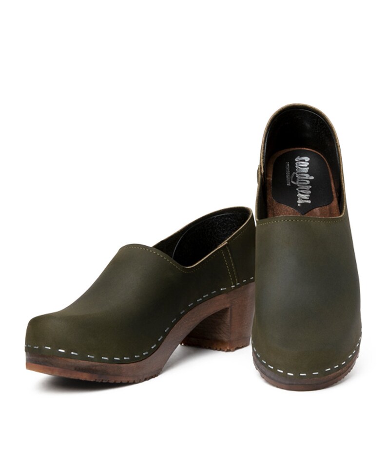 high heeled closed-back clogs in dark green leather on a dark wooden base