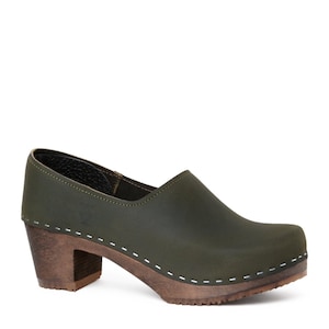 high heeled closed-back clogs in dark green leather on a dark wooden base