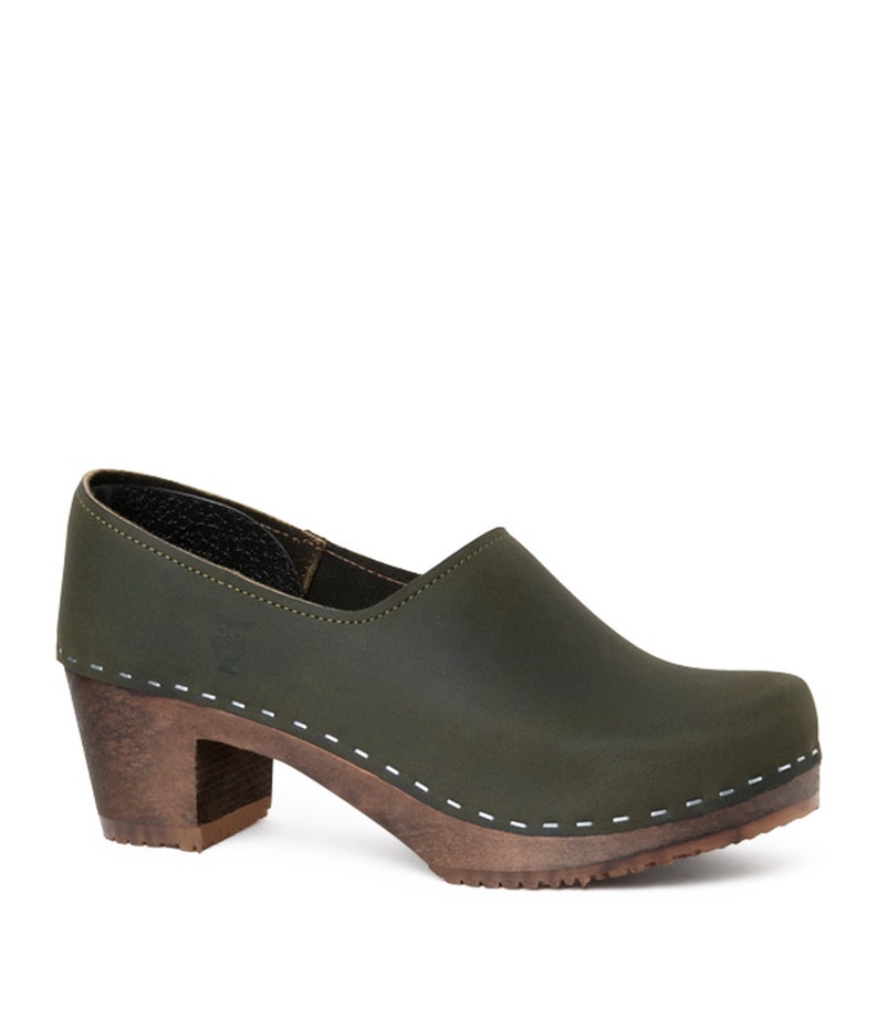 high heeled closed-back clogs in dark green leather on a dark wooden base