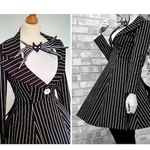 May include: Black and white pinstripe dress with a matching decorative necklace. The dress features a notched collar, long sleeves, and a flared skirt. A single white button accents the waist. The necklace has a bat-like design.
