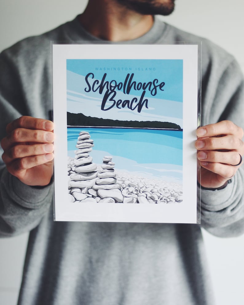 May include: A white print with blue and green accents featuring the text "Schoolhouse Beach" and "Washington Island". The print depicts a beach scene with stacked rocks and a blue body of water.