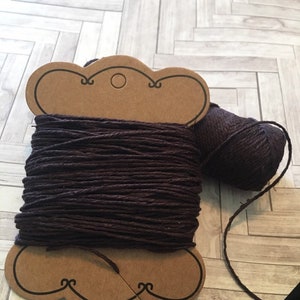 Może przedstawiać: Szpula ciemnofioletowej sznurówki owinięta wokół brązowej kartki z papieru z dziurką na górze. Sznurówka jest również luźna i zwisa ze szpuli.