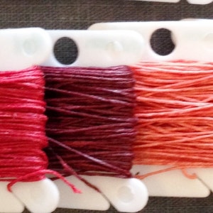 Pode incluir: Seis carretéis de fio para bordar em vários tons de vermelho, laranja e marrom. O fio está enrolado em bobinas de plástico branco.