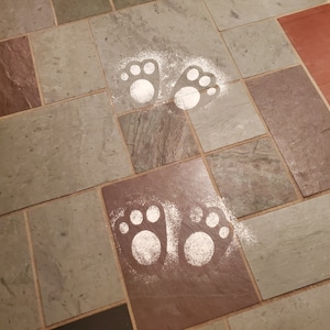 May include: Two sets of white paw prints on a tiled floor. The paw prints are made of a white substance, possibly flour or powdered sugar.