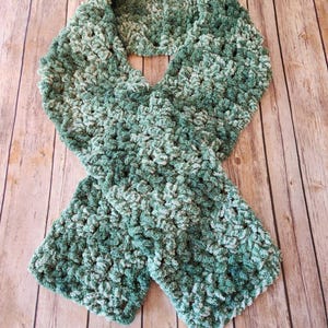 May include: A green and white crocheted infinity scarf. The scarf is made with a soft, fuzzy yarn and has a textured, chunky look.