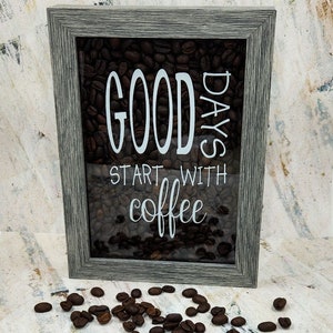 Può includere: Un cartello incorniciato con una cornice in legno grigio e un fronte in vetro. Il cartello è pieno di chicchi di caffè e ha il testo "Good Days Start With Coffee" in lettere bianche.