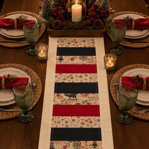 May include: A rectangular table runner featuring alternating horizontal stripes of solid black, solid red, and a beige fabric patterned with snowflakes, Christmas trees, and the text Merry Bright, centered on a wooden dining table with place settings.