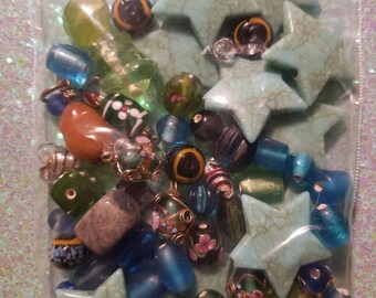 May include: A plastic bag filled with a variety of colorful beads and turquoise star-shaped charms. The beads are made of glass, metal, and plastic. The charms are made of turquoise.