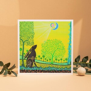 May include: A square art print featuring a black hare silhouette gazing upwards. The background is a vibrant yellow with a crescent moon and sun rays. Green trees and a floral border frame the scene, creating a whimsical, nature-inspired artwork.