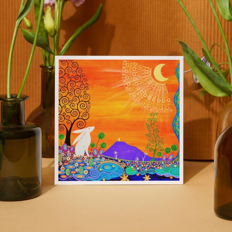 May include: A square art print featuring a white rabbit in a colorful landscape with a purple hill, a stylized tree with black swirls, and a crescent moon in an orange sky. The foreground is filled with intricate blue, green, and pink patterns.