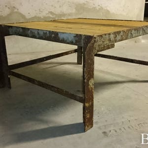 May include: A rusty metal table with a wooden top. The table has a simple design with four legs and a single shelf.