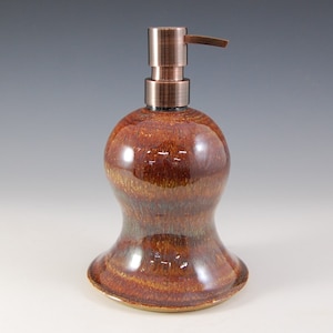 May include: A ceramic soap dispenser with a copper pump. The dispenser has a brown and orange glaze with a slight iridescent sheen.