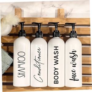 May include: Four white pump bottles with black labels on a bamboo shelf. The labels read "Shampoo", "Conditioner", "Body Wash", and "Face Wash".