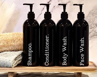 May include: Four black pump bottles with white labels on a wooden shelf. The labels read "Shampoo", "Conditioner", "Body Wash", and "Face Wash".
