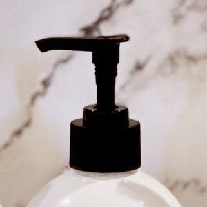 May include: A black pump bottle with a white liquid inside. The pump is made of black plastic and has a long, thin spout.